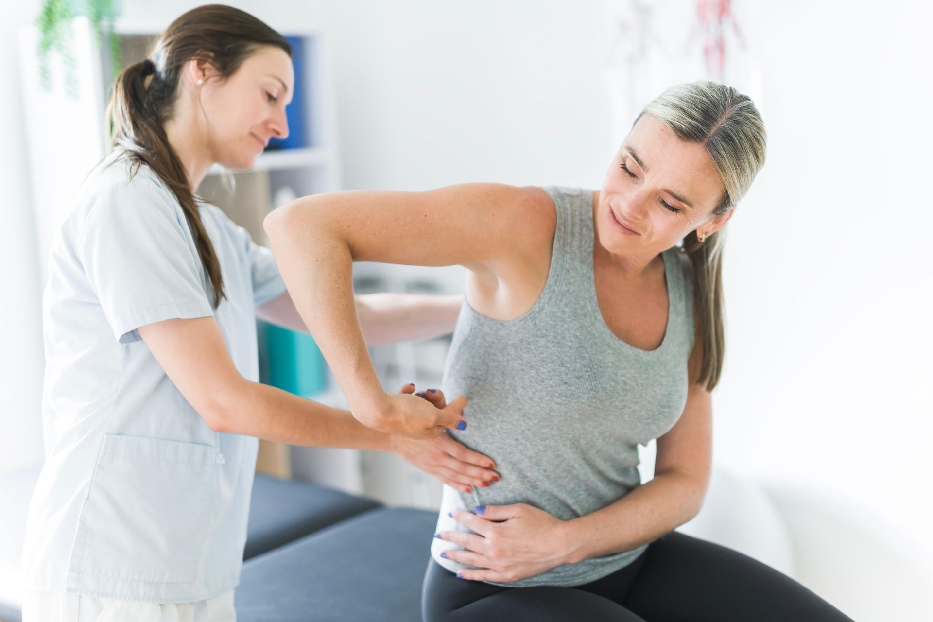 Nurse helping a patient hold her lower back in a bright clinic room