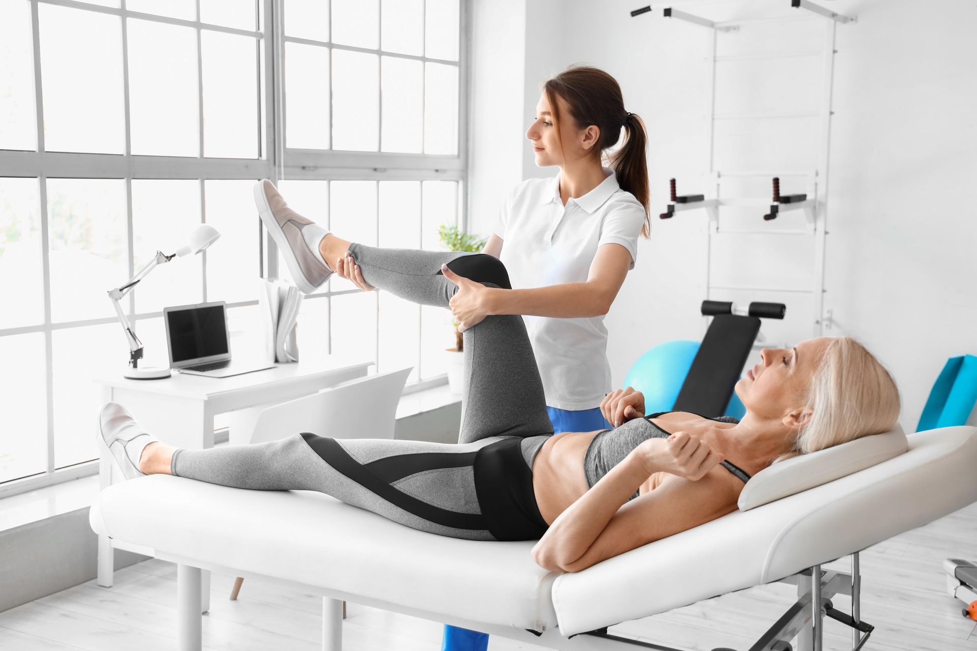 Physical therapist stretching a patient's leg on a treatment table in a bright clinic