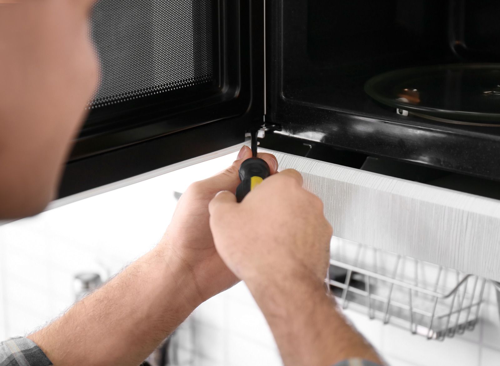 A man is fixing a microwave with a screwdriver.