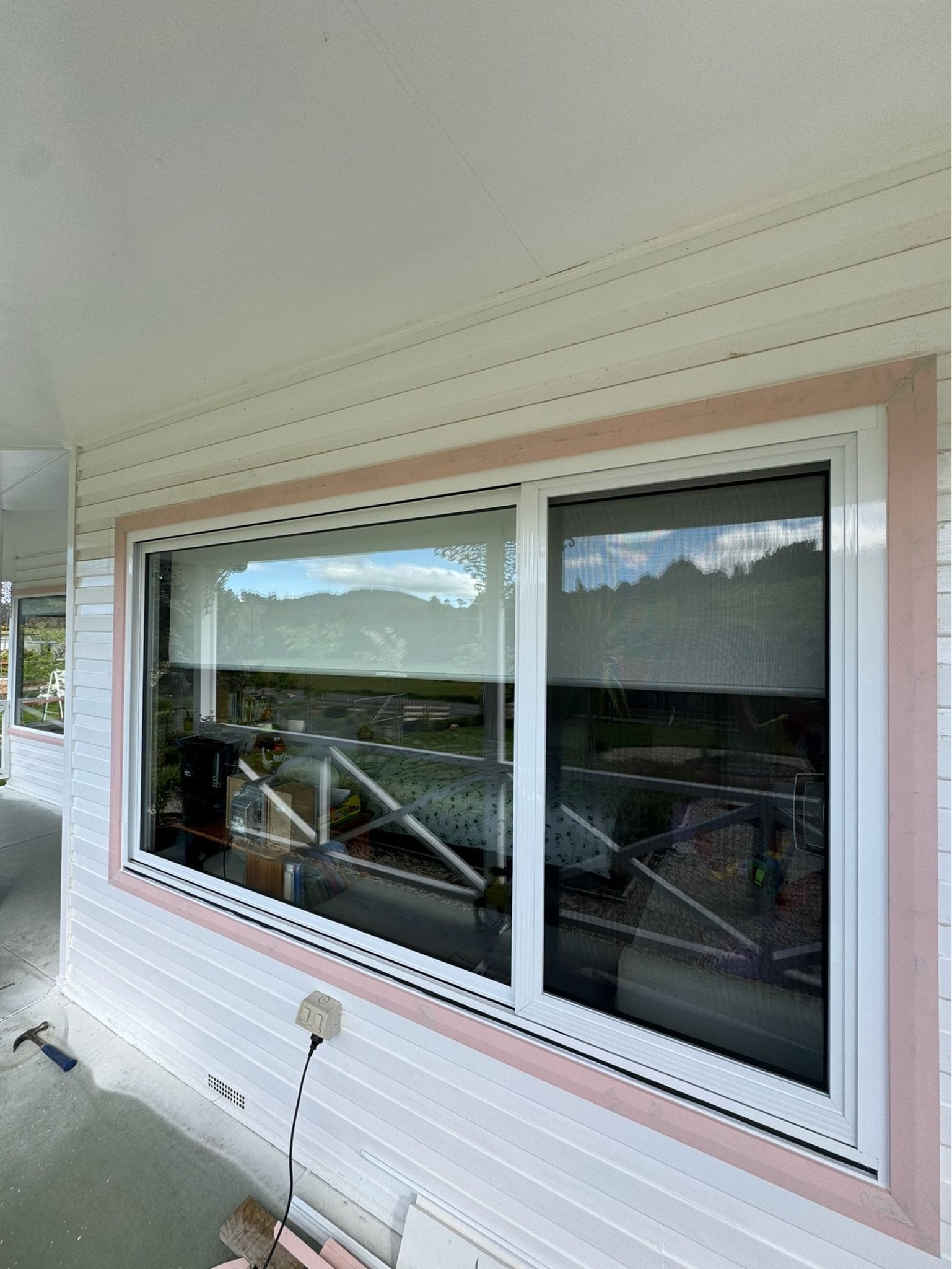 A white horizontal sliding window with a pink frame, installed on the side of a white house. — Channel Glazing In Electrona, TAS