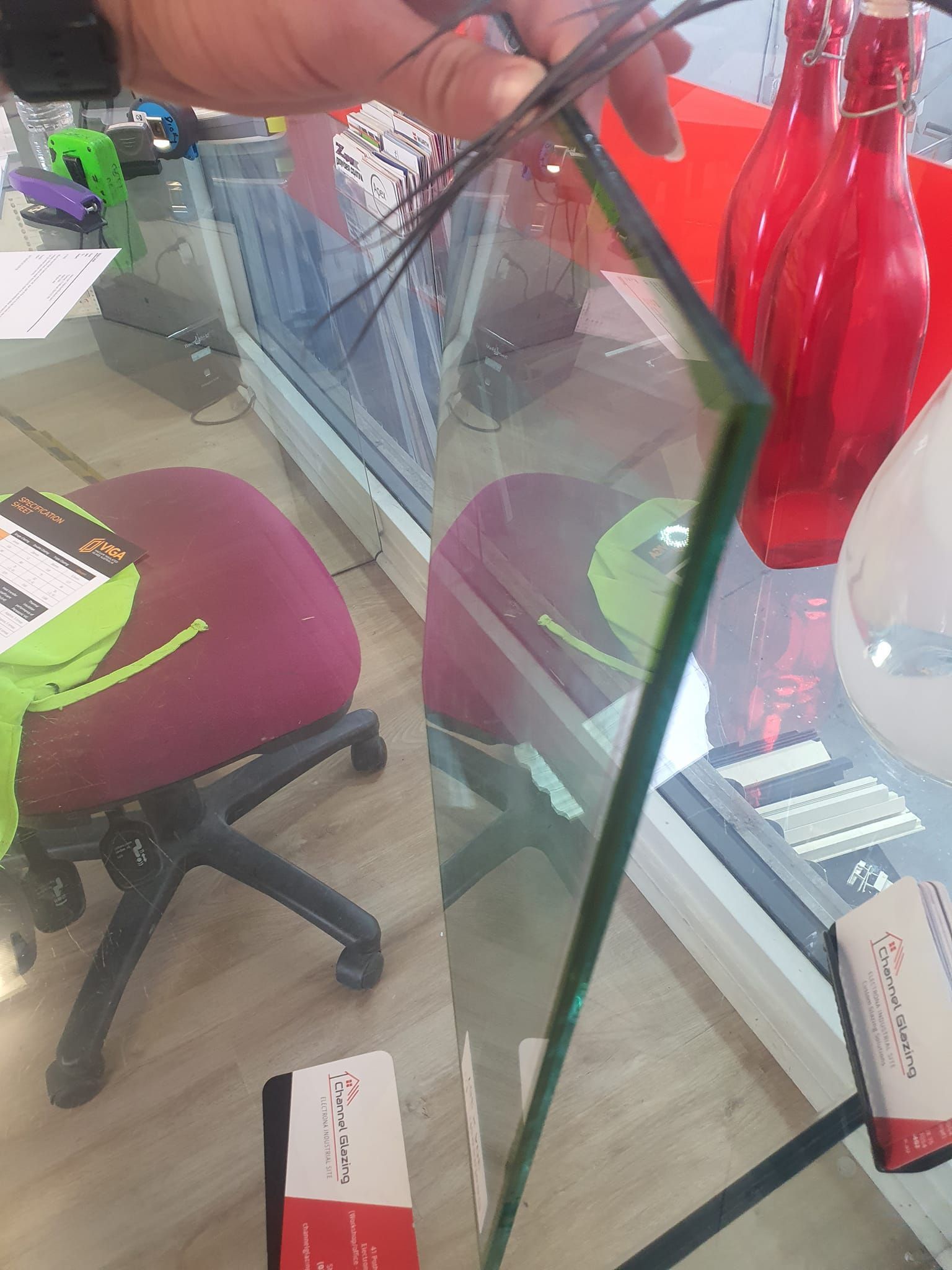 Hand holding a glass shelf panel beside a red vase in a furniture showroom. — Channel Glazing In Electrona, TAS