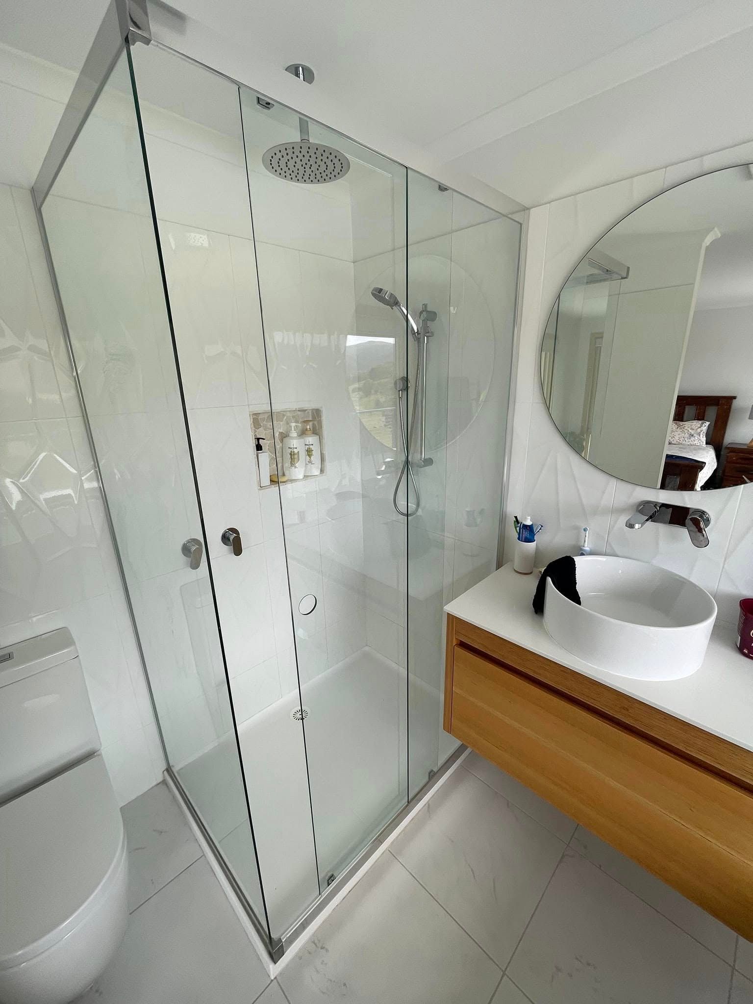 Modern bathroom with a glass-enclosed corner shower, white tiled walls, a wooden vanity, and a round vessel sink. — Channel Glazing In Electrona, TAS