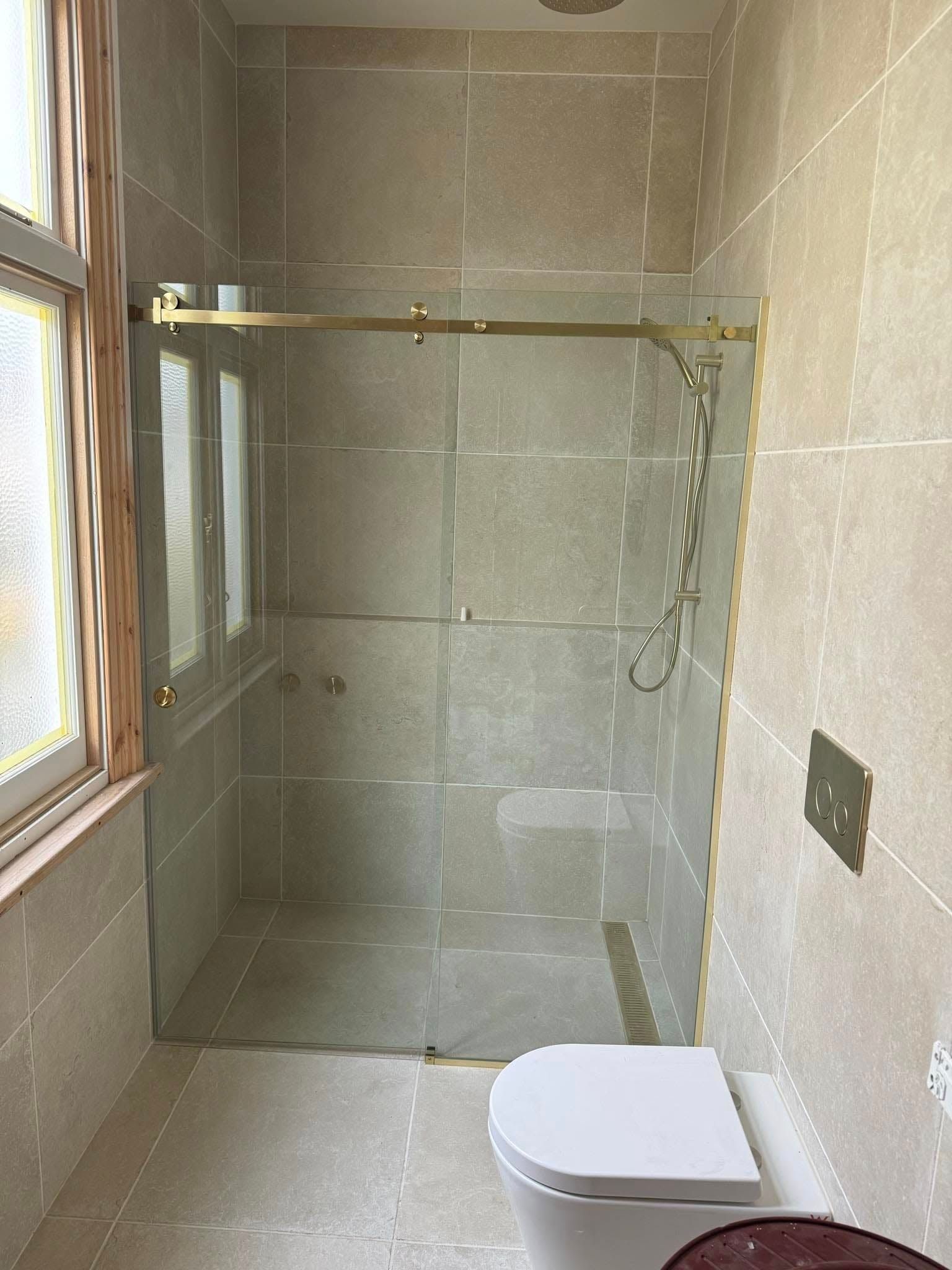 Small tiled bathroom with a glass shower enclosure, window, and toilet.