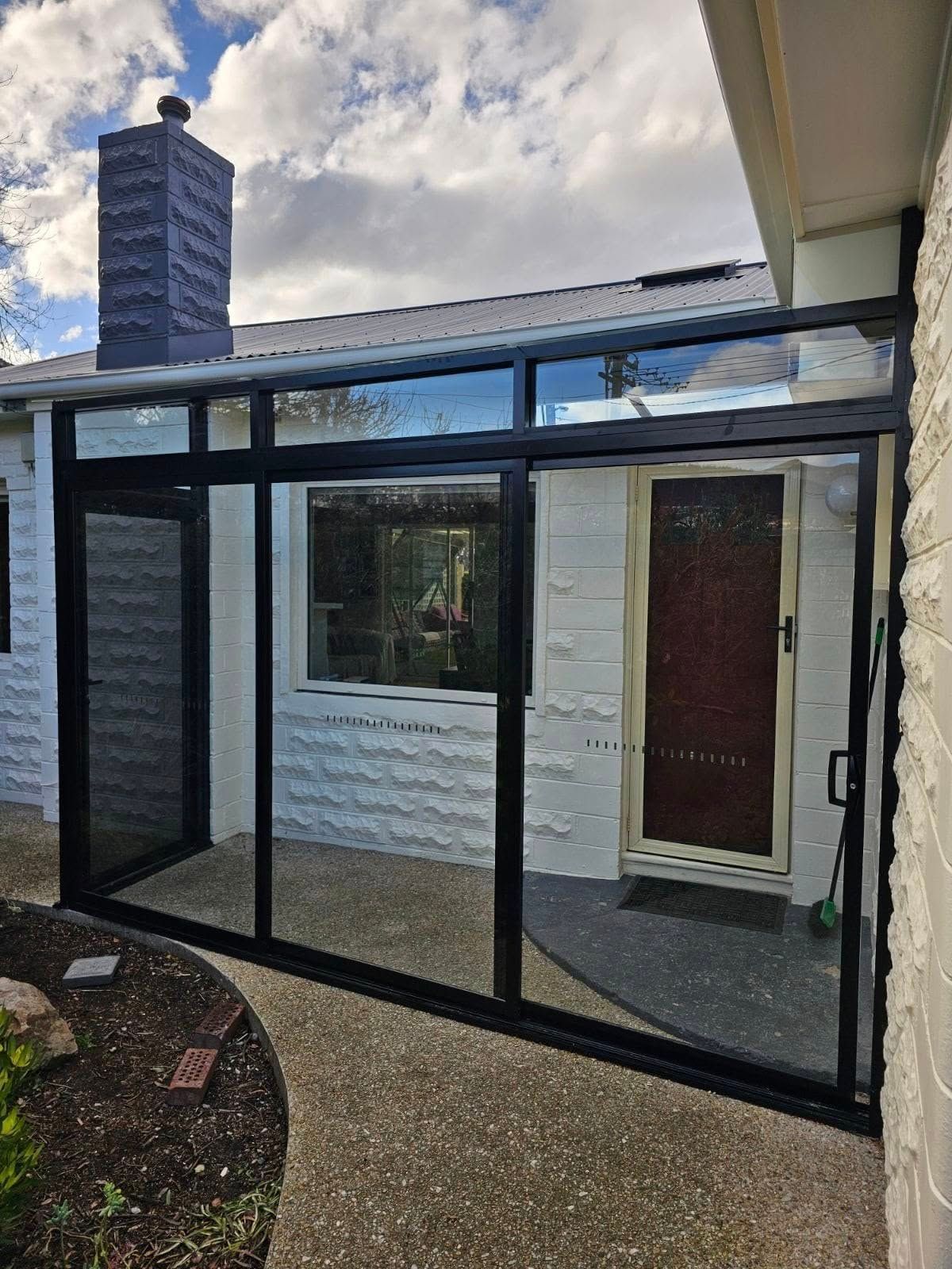 Glass-enclosed porch attached to a white house, with a red door and neighboring chimney visible. — Channel Glazing In Electrona, TAS