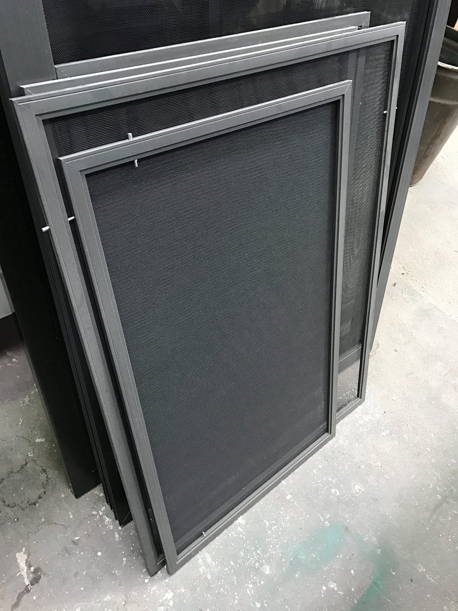 Stacked black mesh window screens leaning against a wall outdoors — Channel Glazing In Electrona, TAS