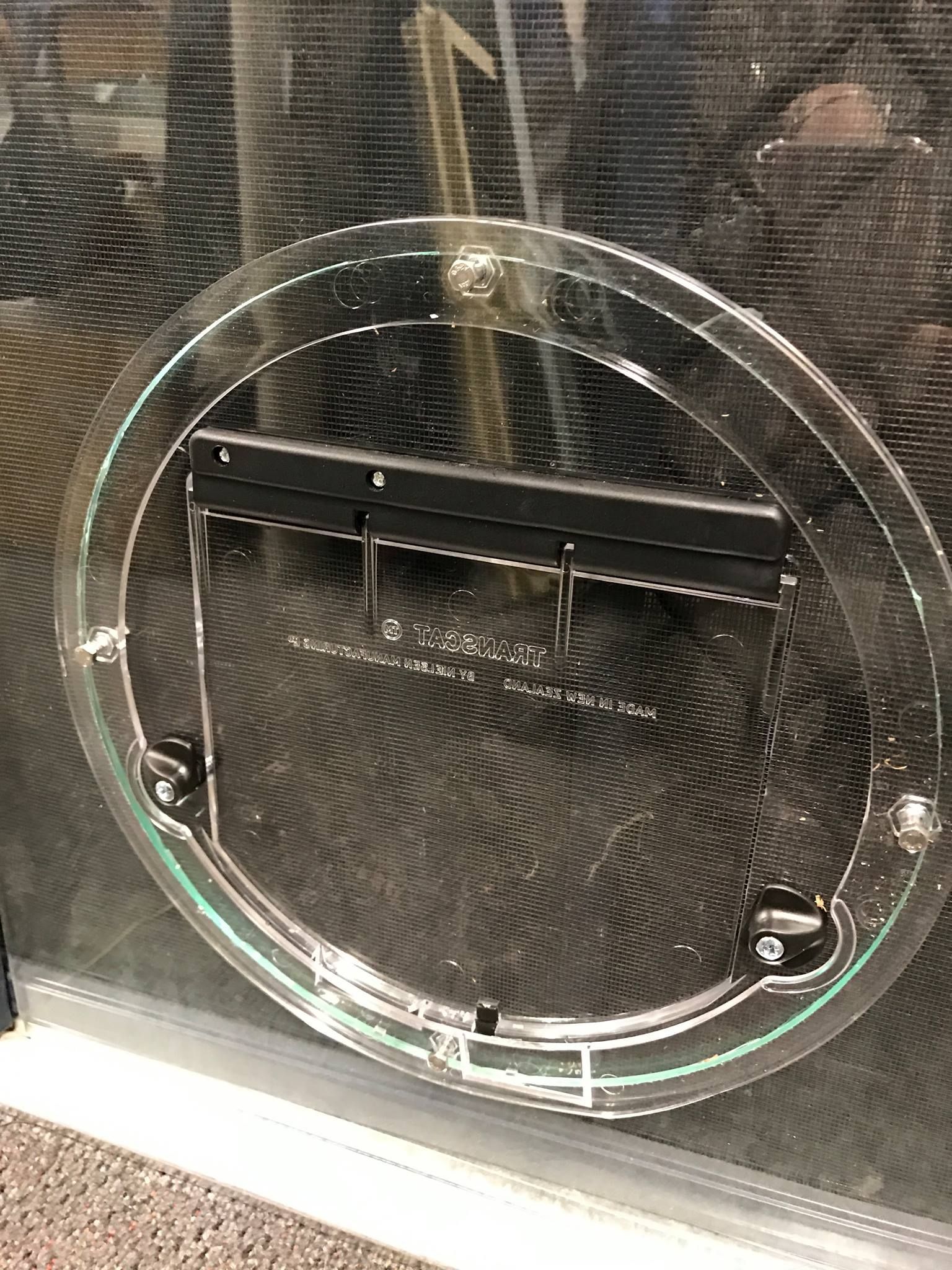 A circular pet door installed in a glass door with a transparent frame and a black swinging flap. — Channel Glazing In Electrona, TAS