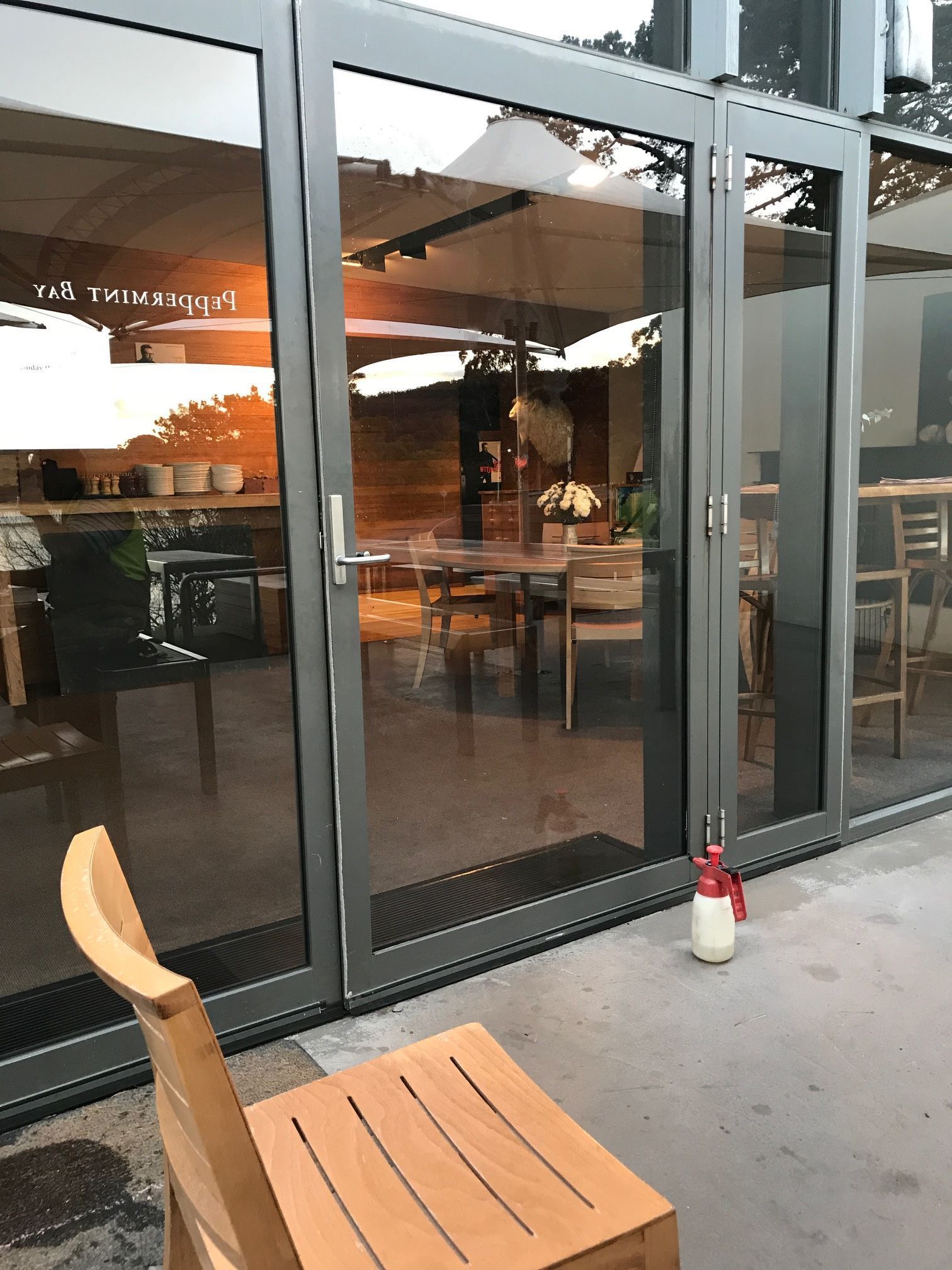 Outdoor café seating beside glass storefront doors, with wooden chairs and a red bottle on the ground. — Channel Glazing In Electrona, TAS