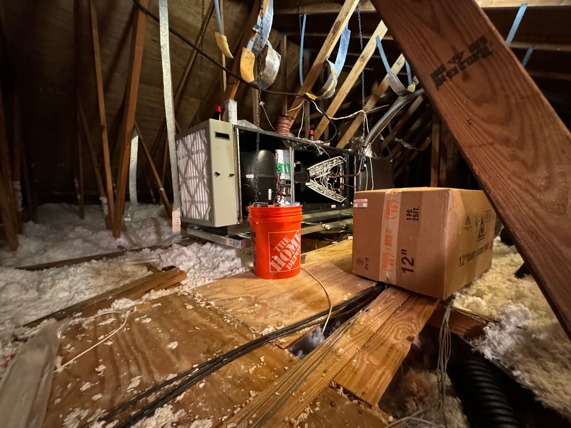 Attic with exposed beams, insulation, ducts, a cardboard box, and an orange bucket on the floor.