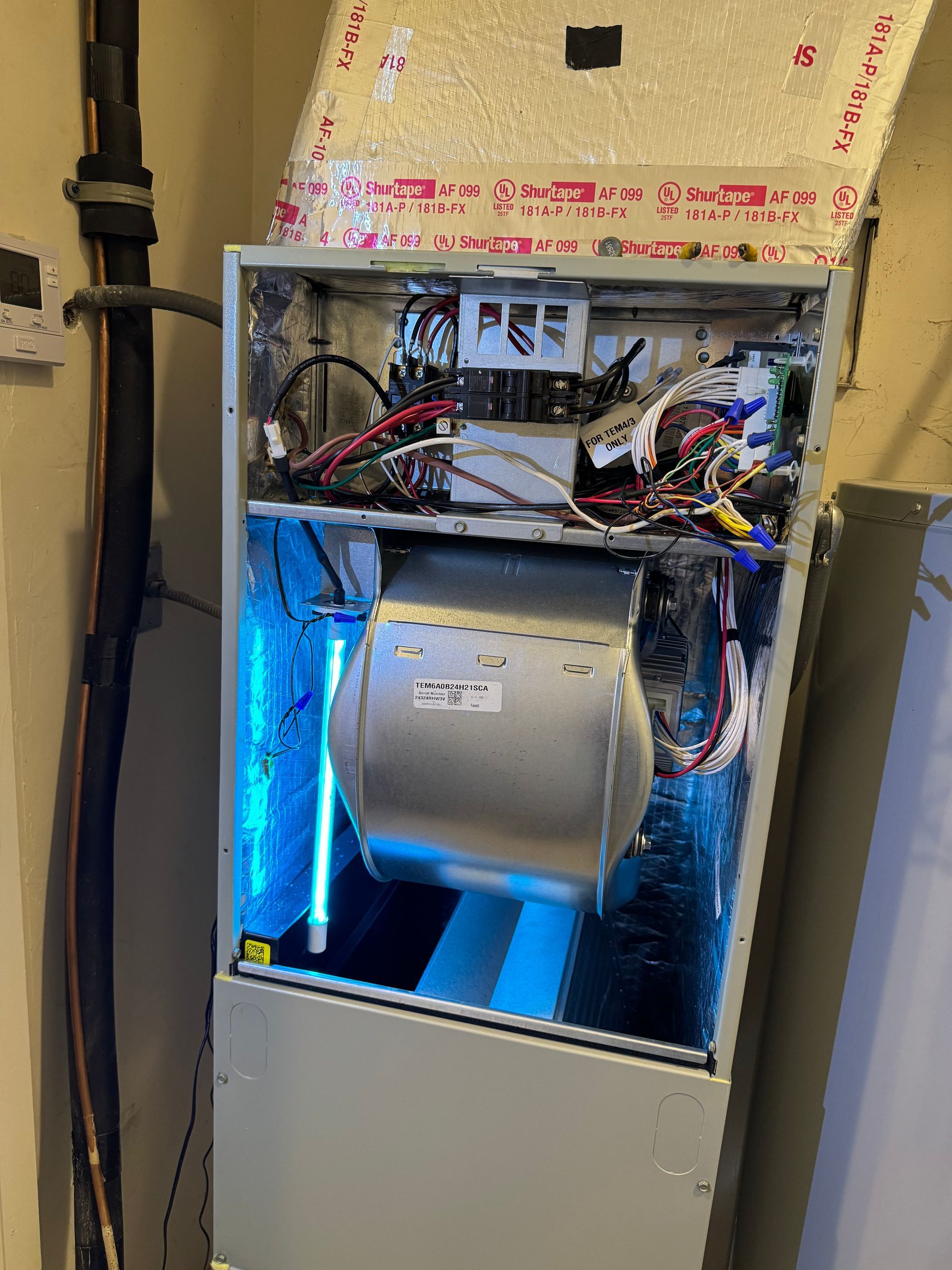 Open electrical panel with exposed wiring and a blue-lit motor or blower inside