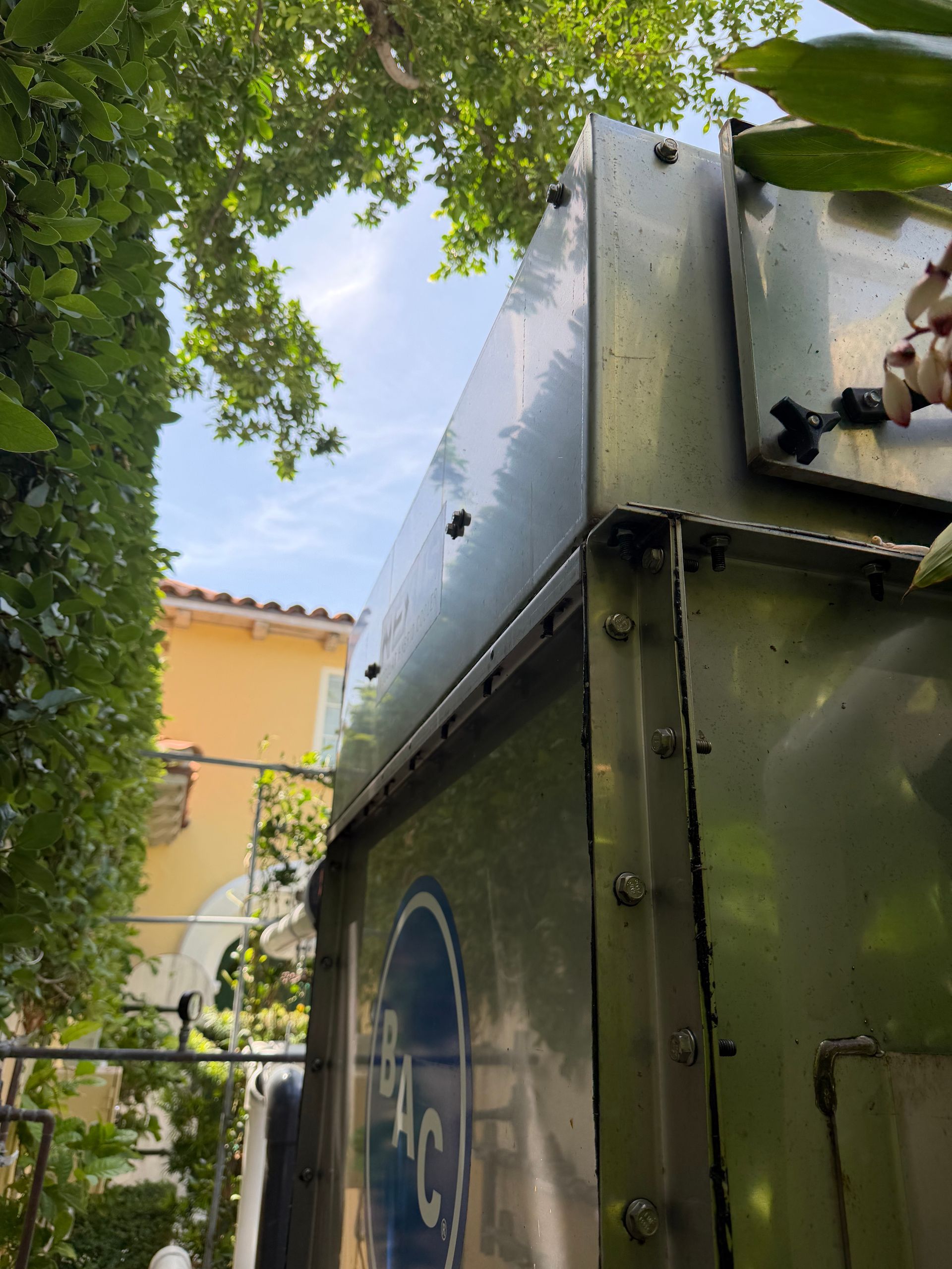 Green metal utility box under trees with a yellow building in the background