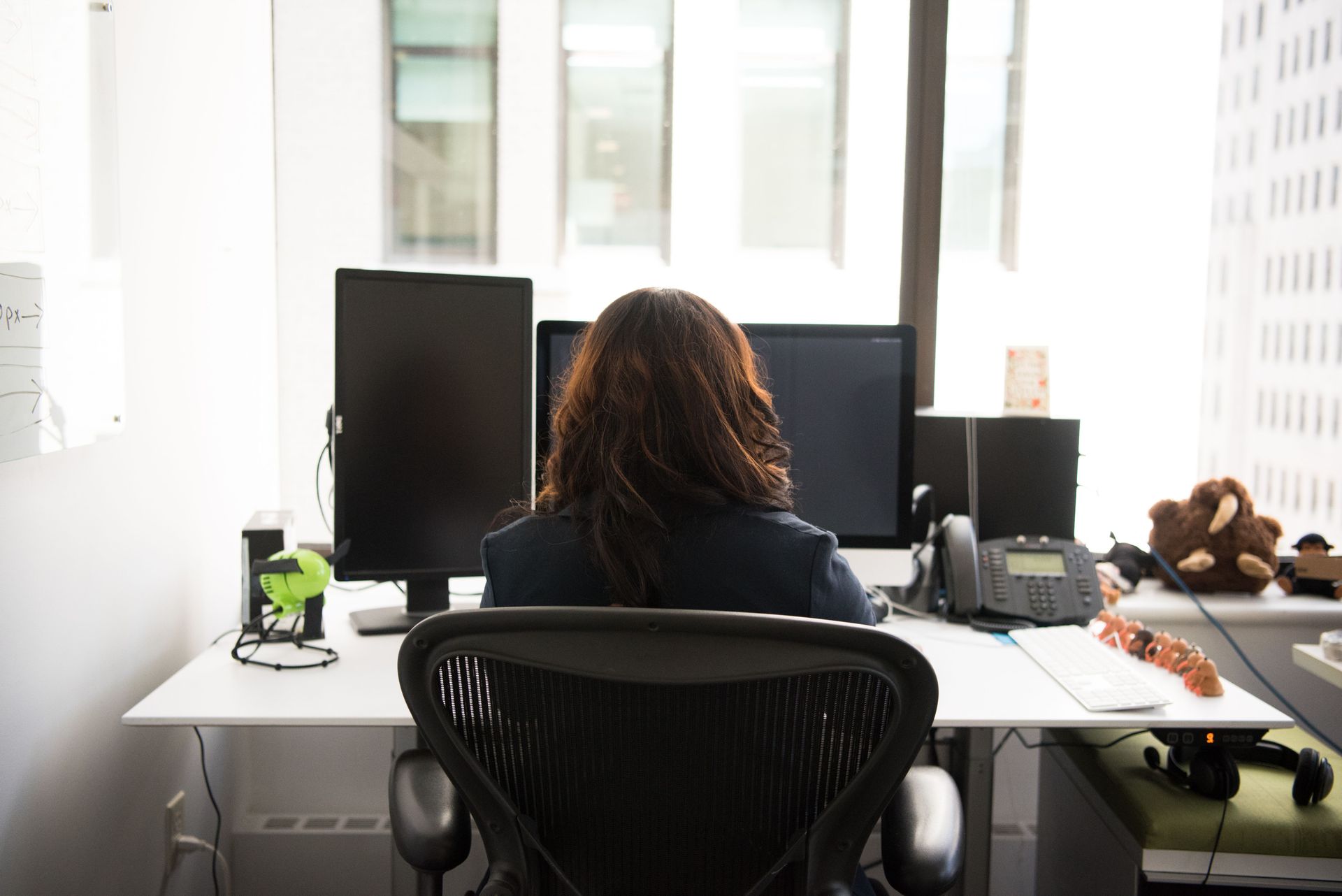 Person seated at a desk facing dual monitors in a bright office workspace
