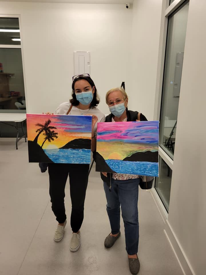 Two women wearing face masks are holding paintings in a room.