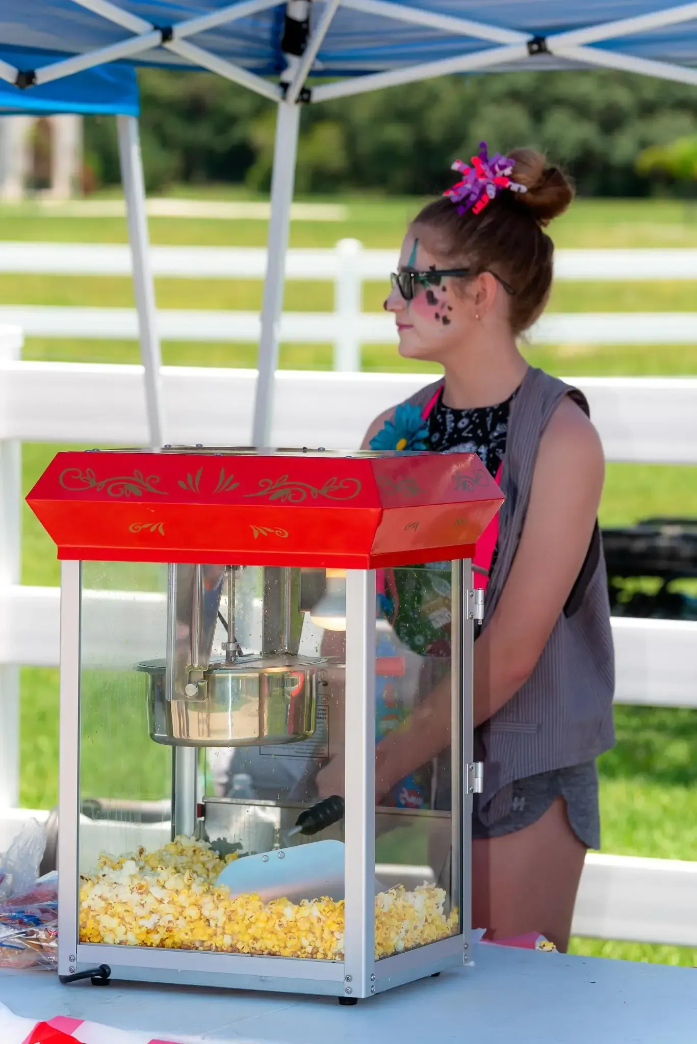 A young girl is standing in front of a popcorn machine.
