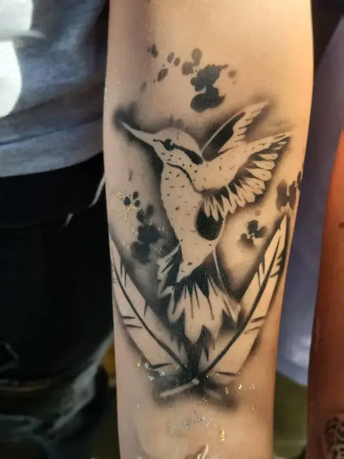 A tattoo of a hummingbird and feathers on a person 's arm