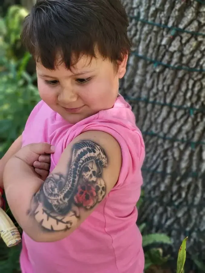 A little girl with a tattoo on her arm is holding a brush.