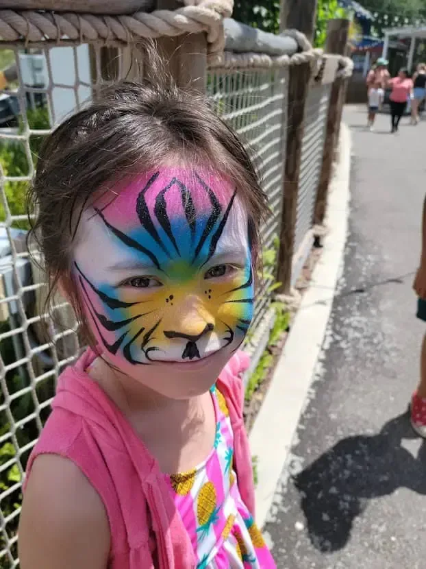 A little girl with her face painted like a tiger.