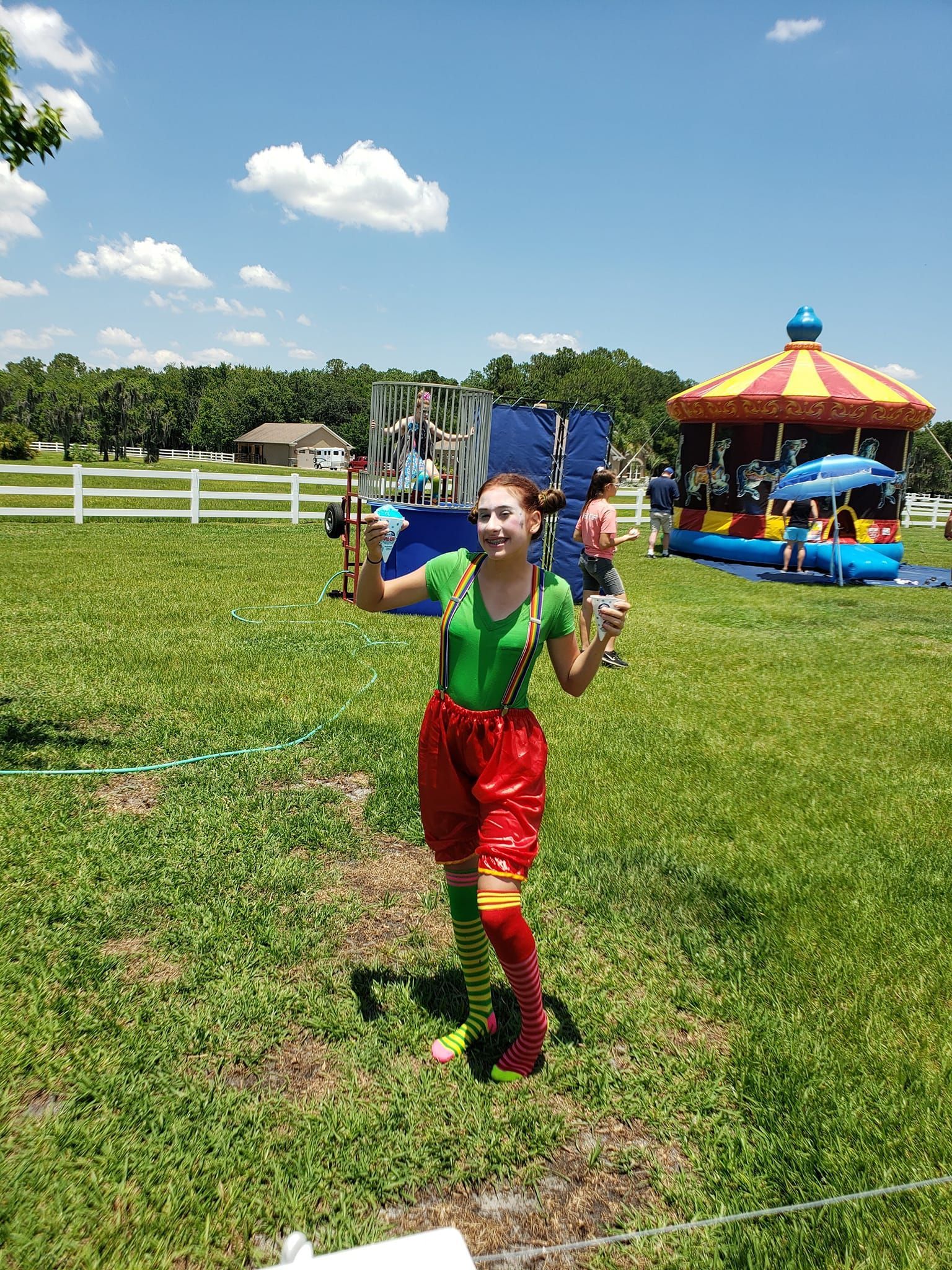 A girl in a clown costume is standing in a grassy field.