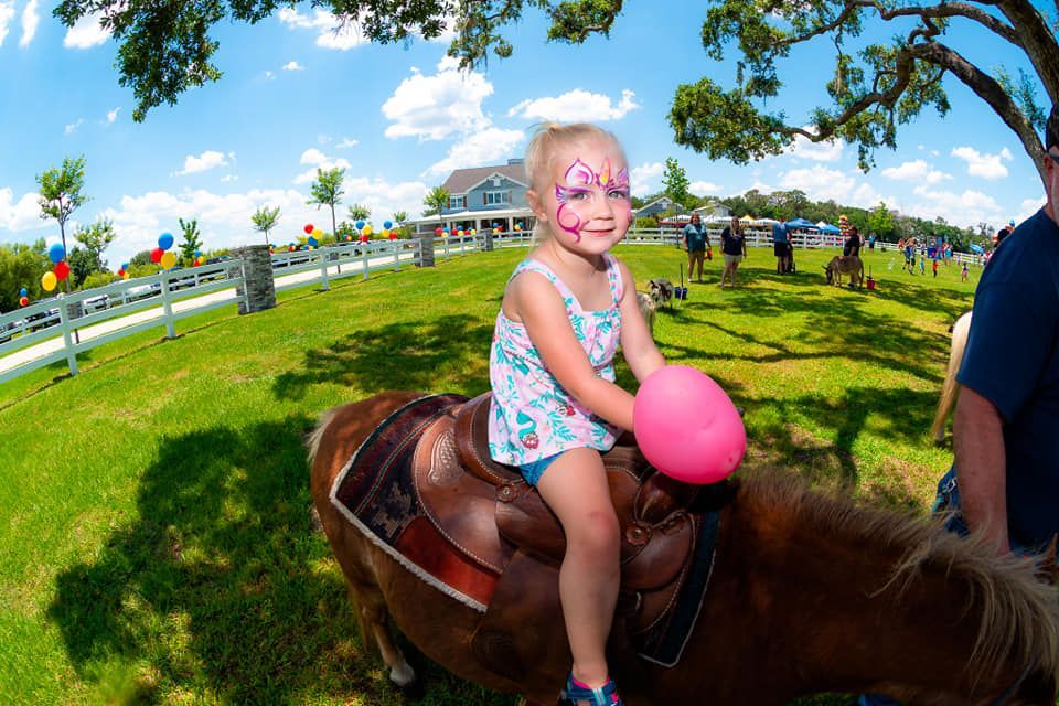 A little girl is riding a pony with a pink ball in her hand.
