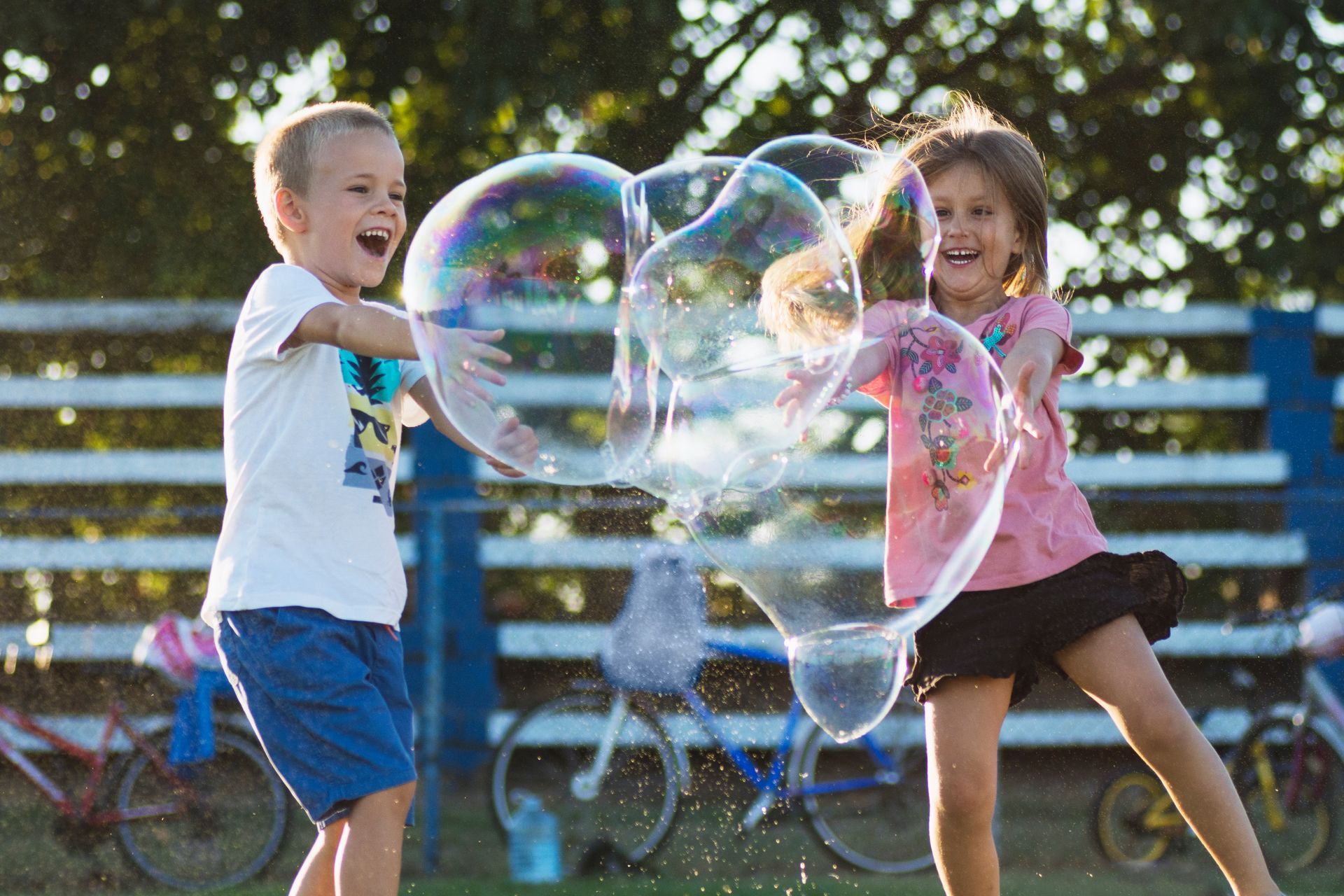 A boy and a girl are playing with soap bubbles in a park.
