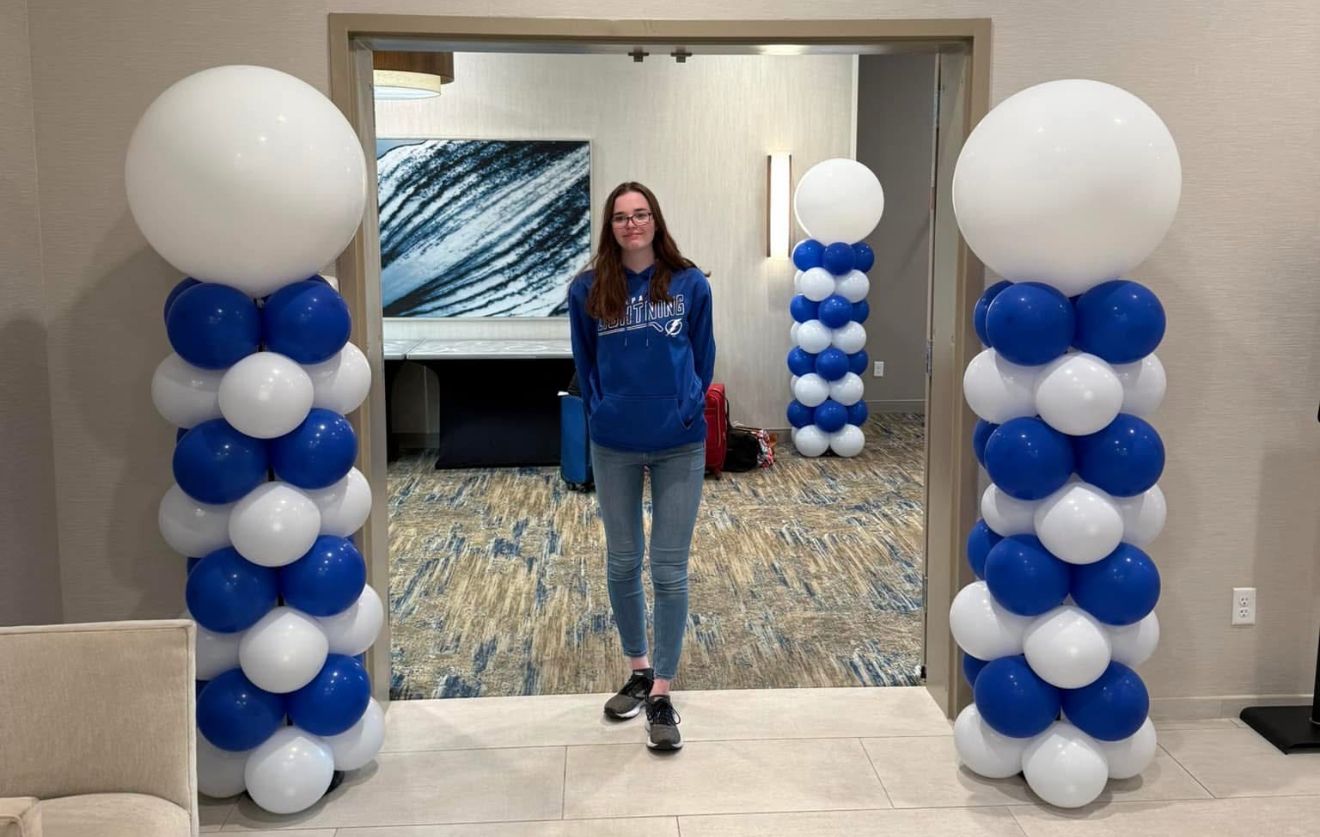 Woman standing between blue and white balloon columns in a hallway.