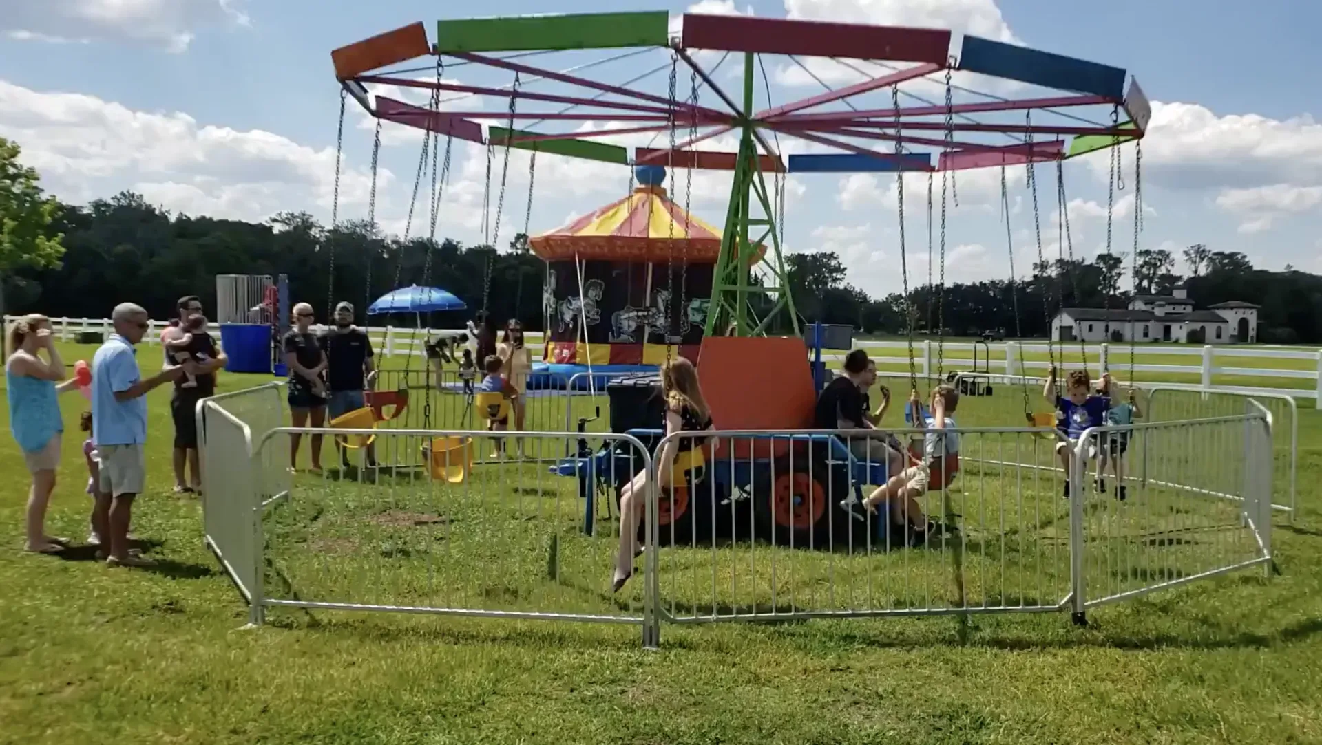 A group of people are standing around a merry go round in a park.