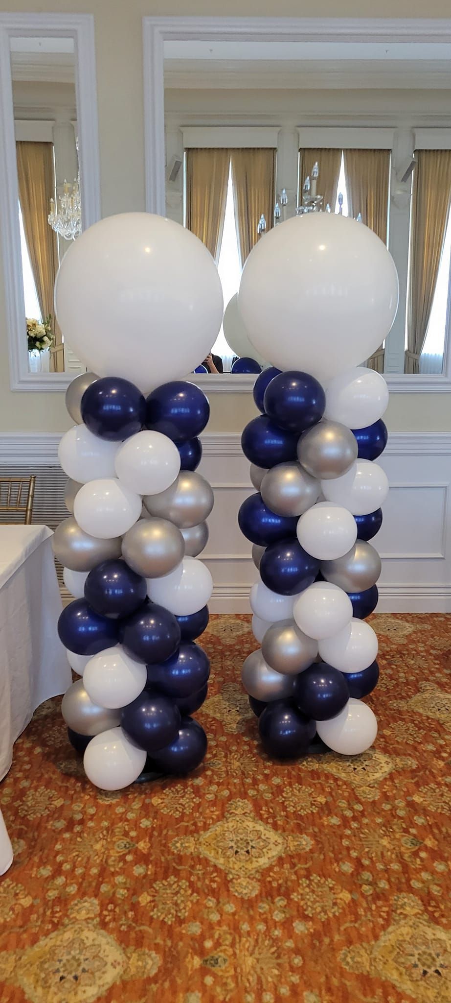 Two columns made of blue , white , and silver balloons in a room.