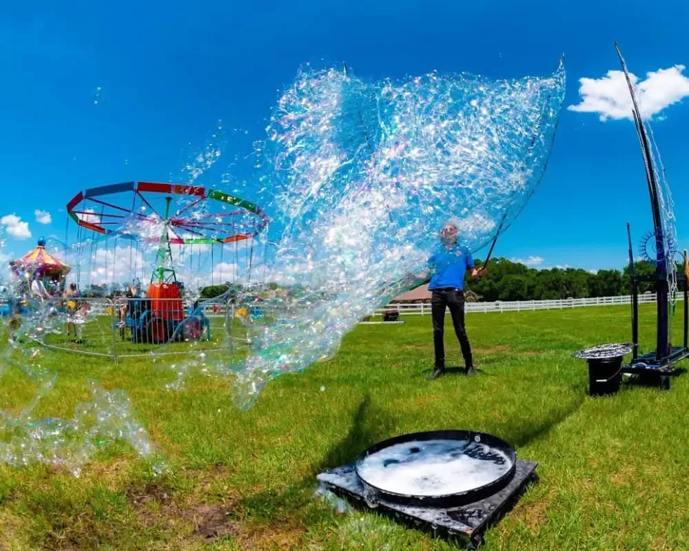 A man is blowing soap bubbles in a field at a carnival.