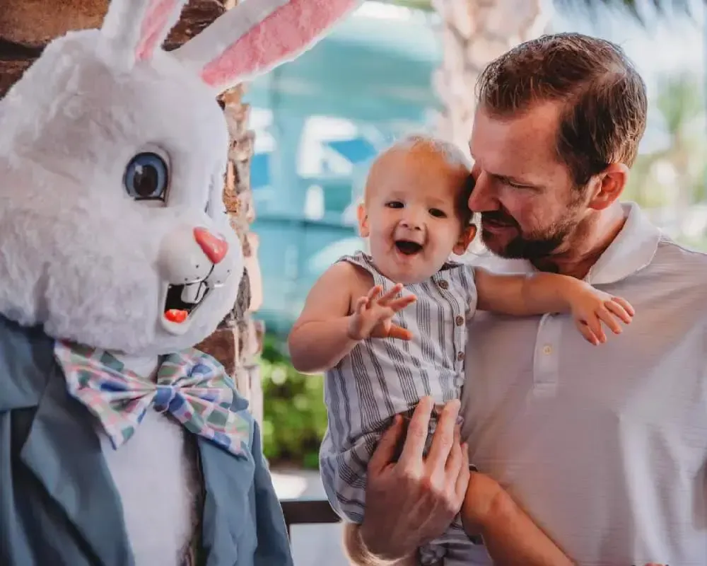 A man is holding a baby next to a stuffed bunny rabbit.