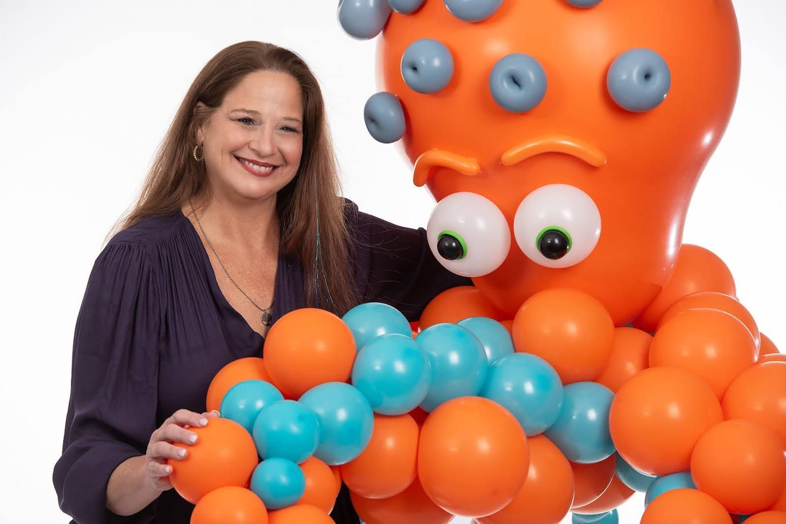 A woman is standing next to an octopus made of balloons.