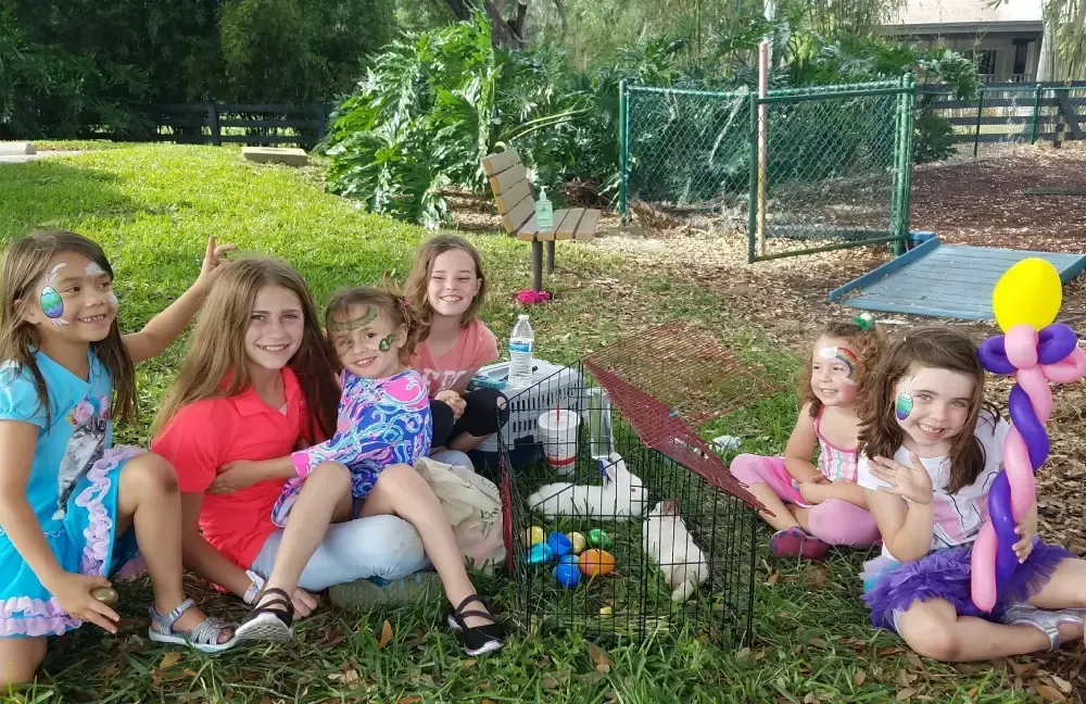 A group of young girls are sitting in the grass with balloons on their faces.