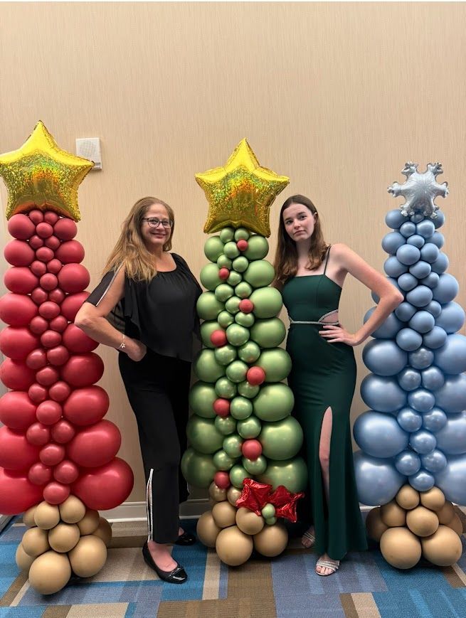 Flat balloon sculptures shaped like Christmas trees in red, green, and blue topped with stars and snowflake