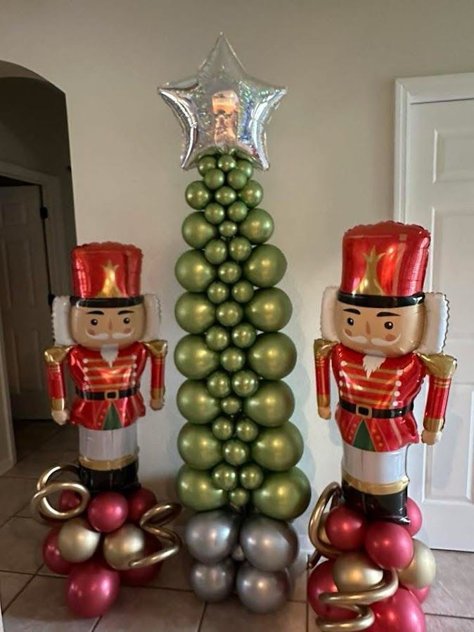 Nutcracker foil balloons flanking a tall, green flat balloon Christmas tree with a star topper.