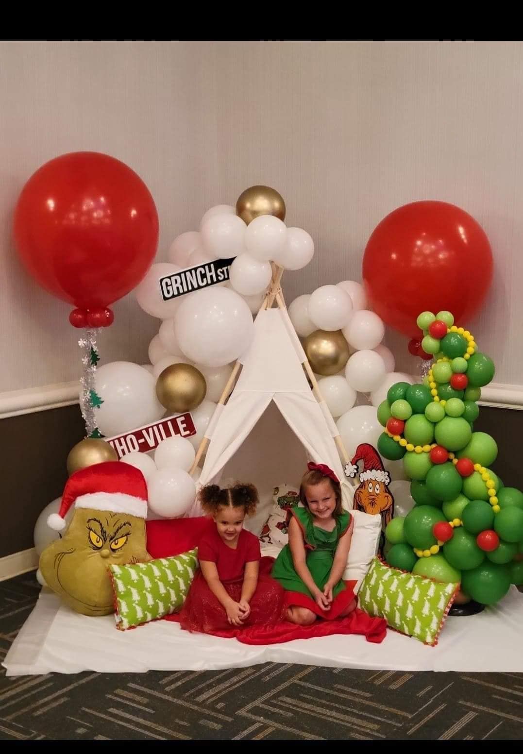 Two little girls are sitting in a teepee surrounded by balloons.