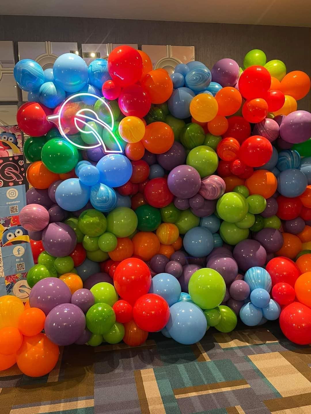A wall filled with lots of colorful balloons and a neon sign.