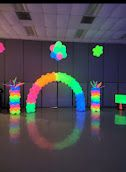 Neon-colored balloon arch and columns glowing in a dark room under black light, featuring a colorful overhead floral shape.