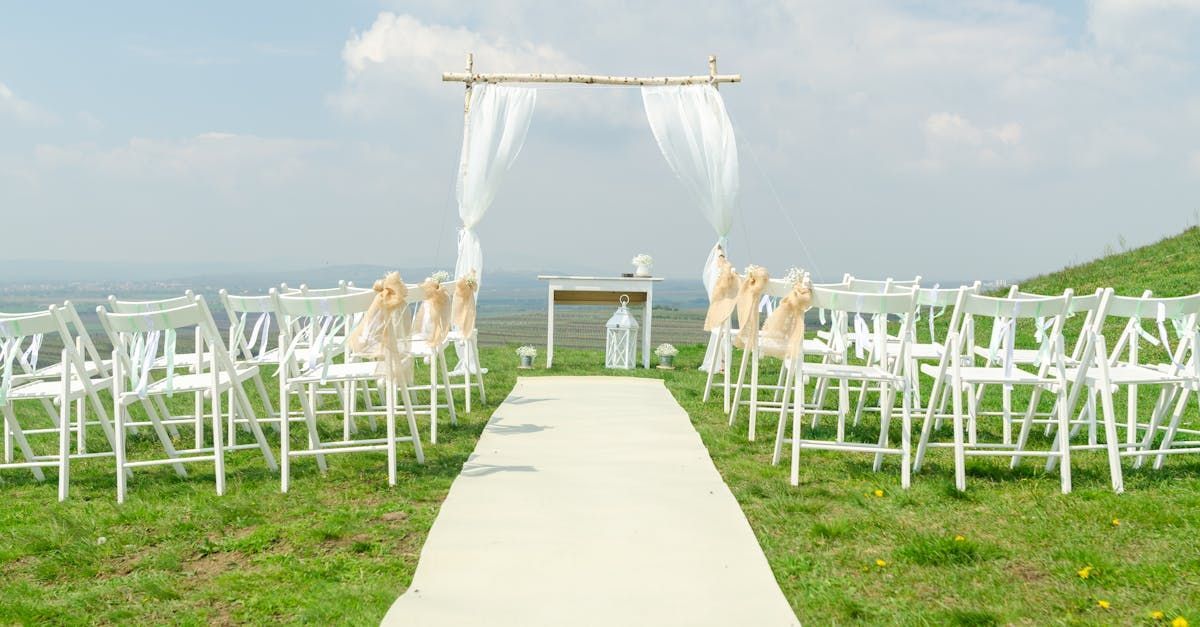 A row of white chairs are lined up in a field for a wedding ceremony.