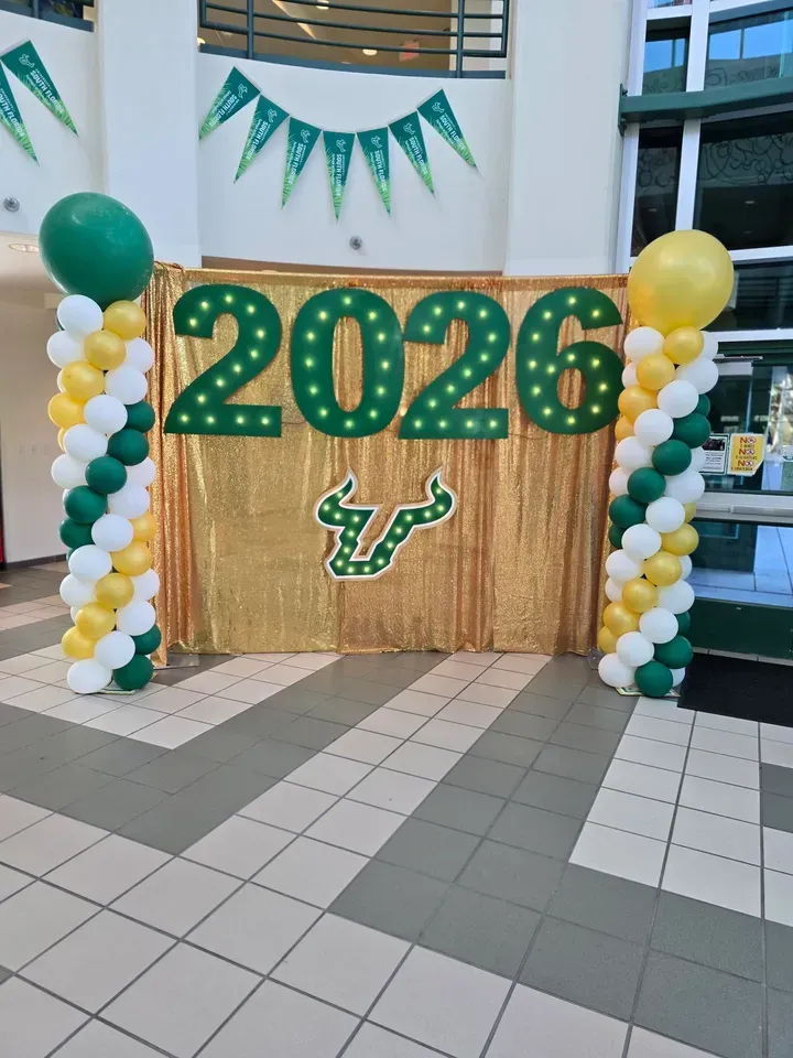 Green and gold 2026 balloon display with USF logo, flanked by balloon columns in a lobby