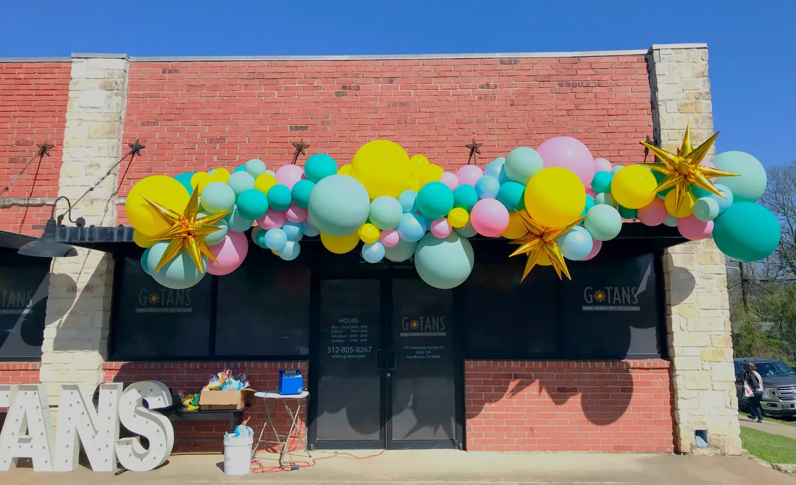 A colorful balloon garland is hanging over a brick building.
