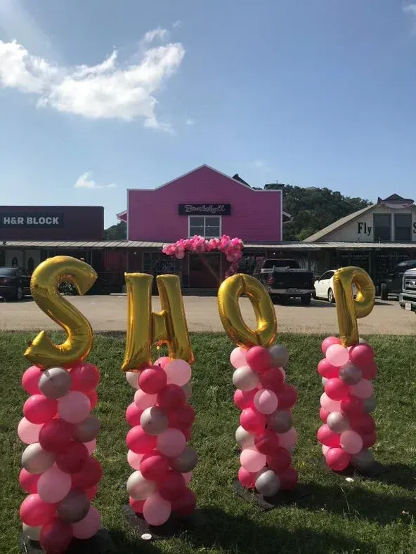 The word shop is made out of balloons in front of a pink building.
