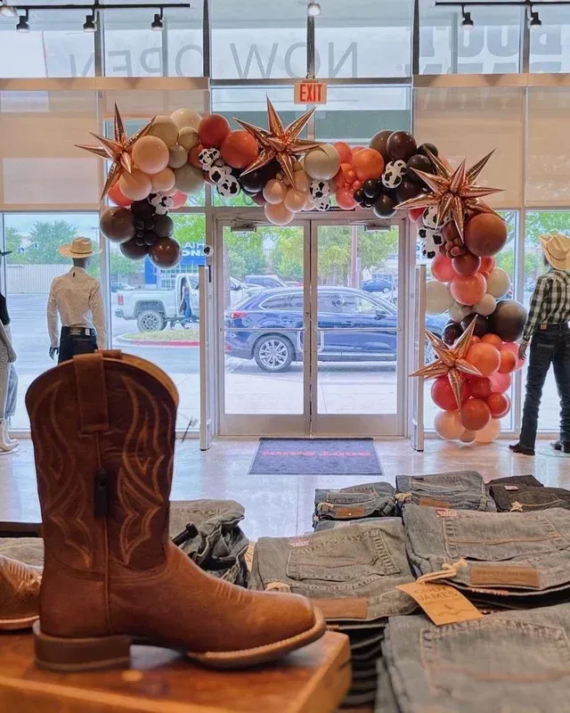 A cowboy boot is on display in a store with balloons in the background.