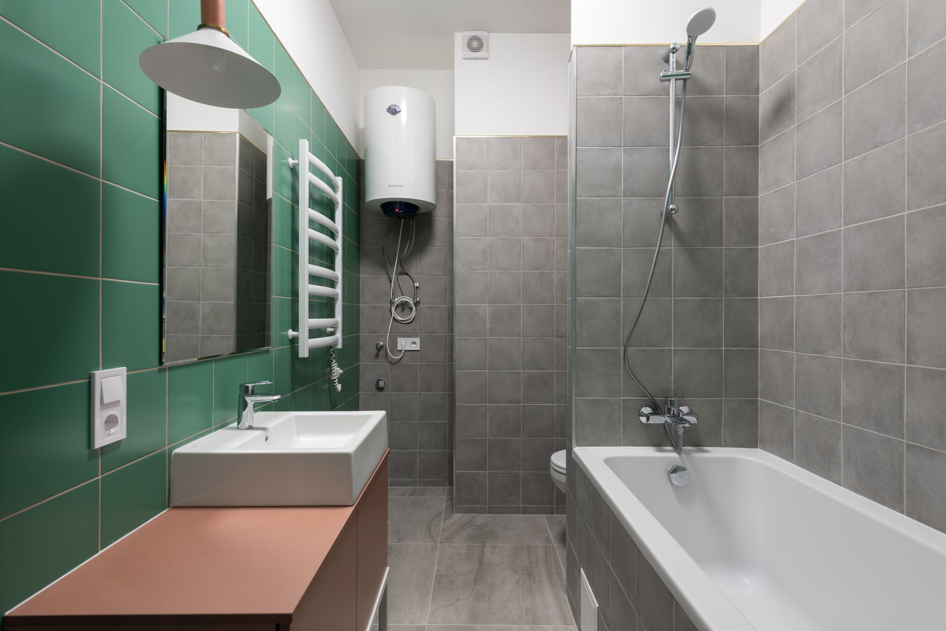Modern bathroom with green tile accent wall, bathtub, sink, mirror, towel rack, and wall-mounted water heater