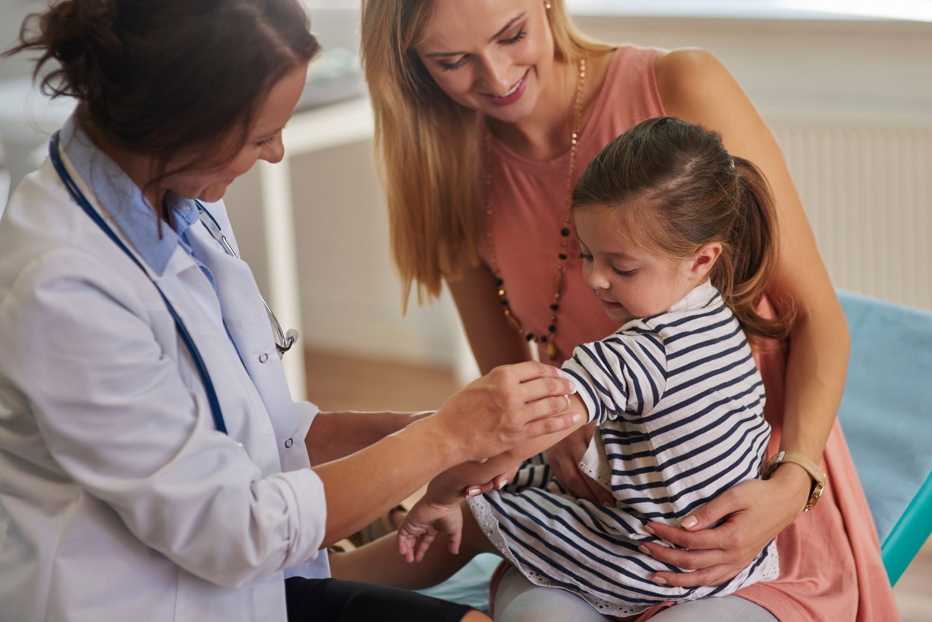 Doctor examining a child’s hand while a parent comforts her in a clinic.