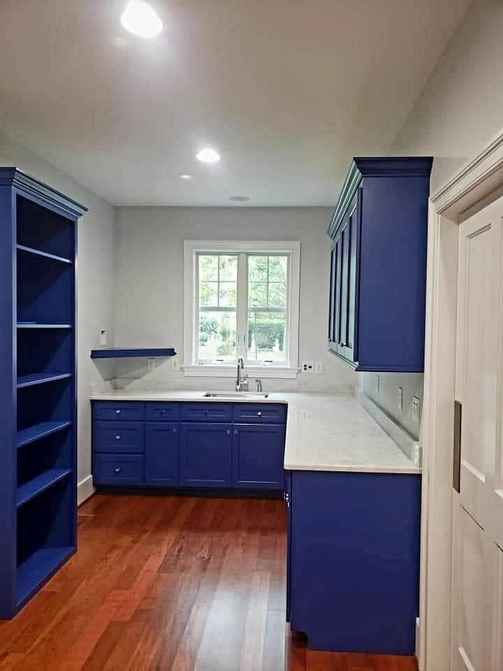 Blue kitchen with white countertops, window over sink, hardwood floor, and open shelving.