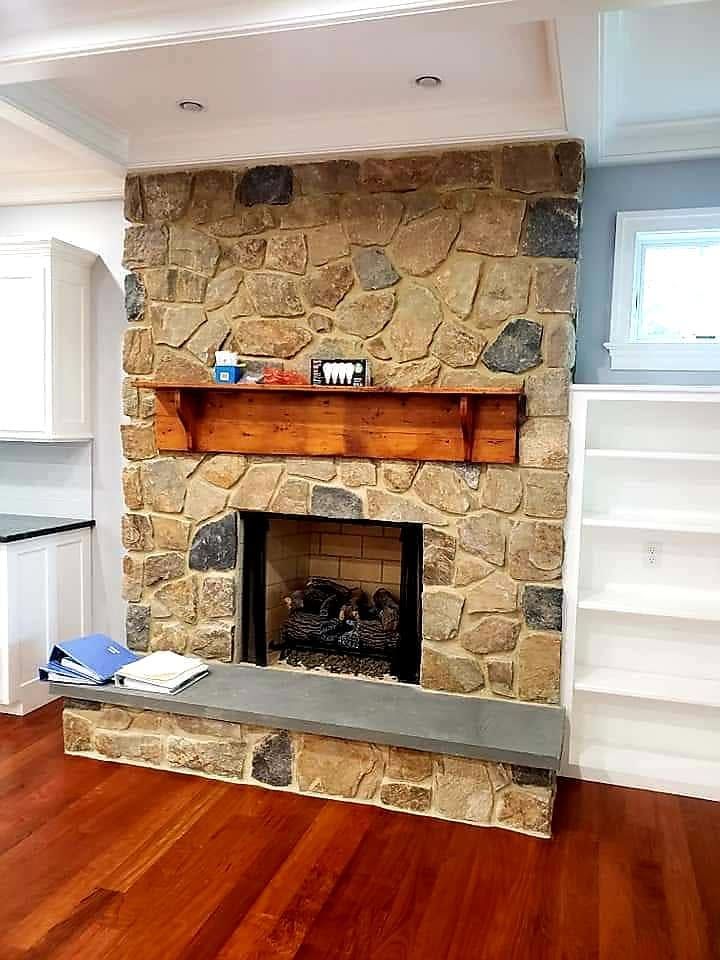 Stone fireplace with wooden mantel and gray hearth in a bright room with hardwood floors