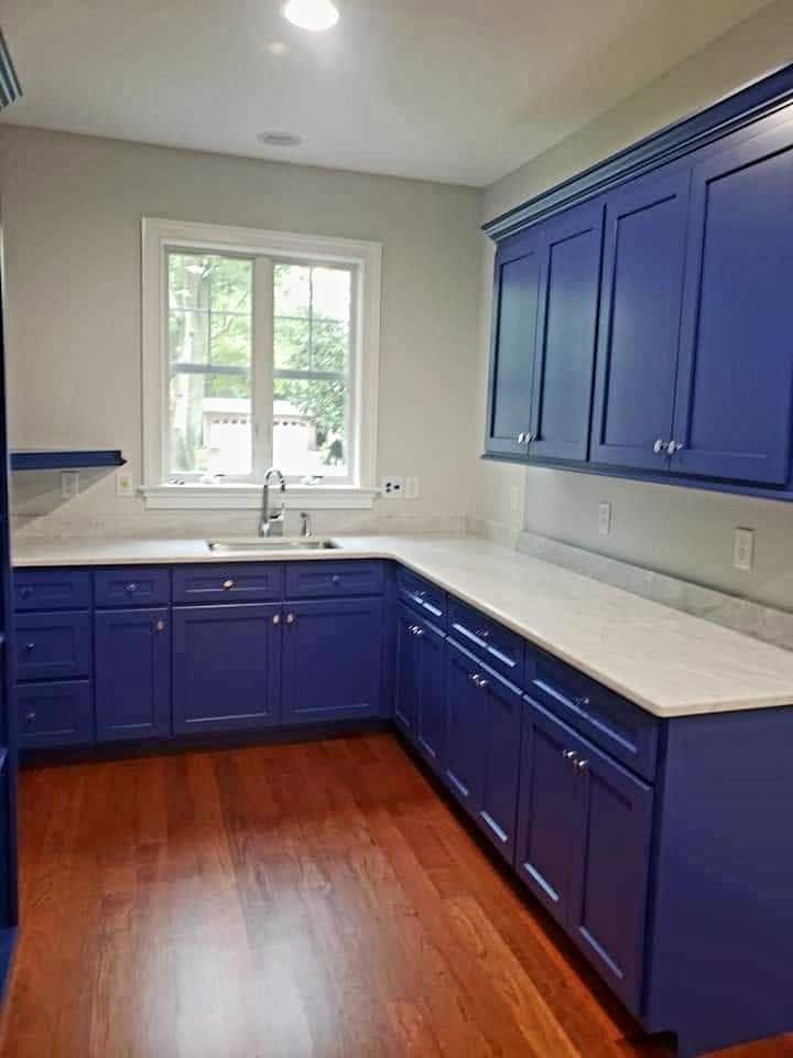 Blue kitchen with white countertops, wood floor, and a window above the sink.