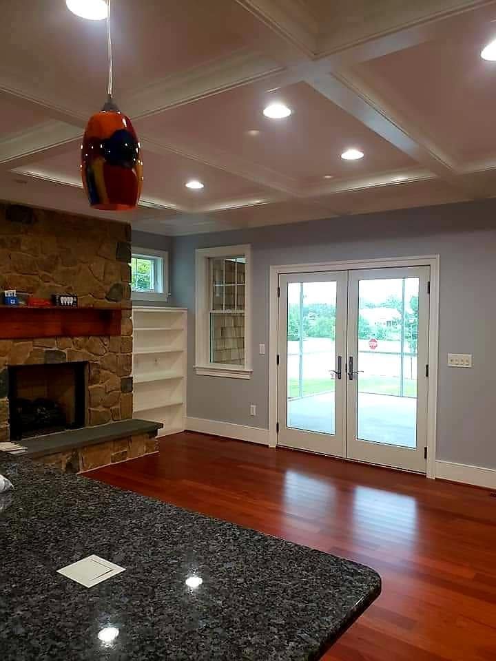 Bright kitchen with granite island, fireplace, hardwood floors, and French doors to a backyard.