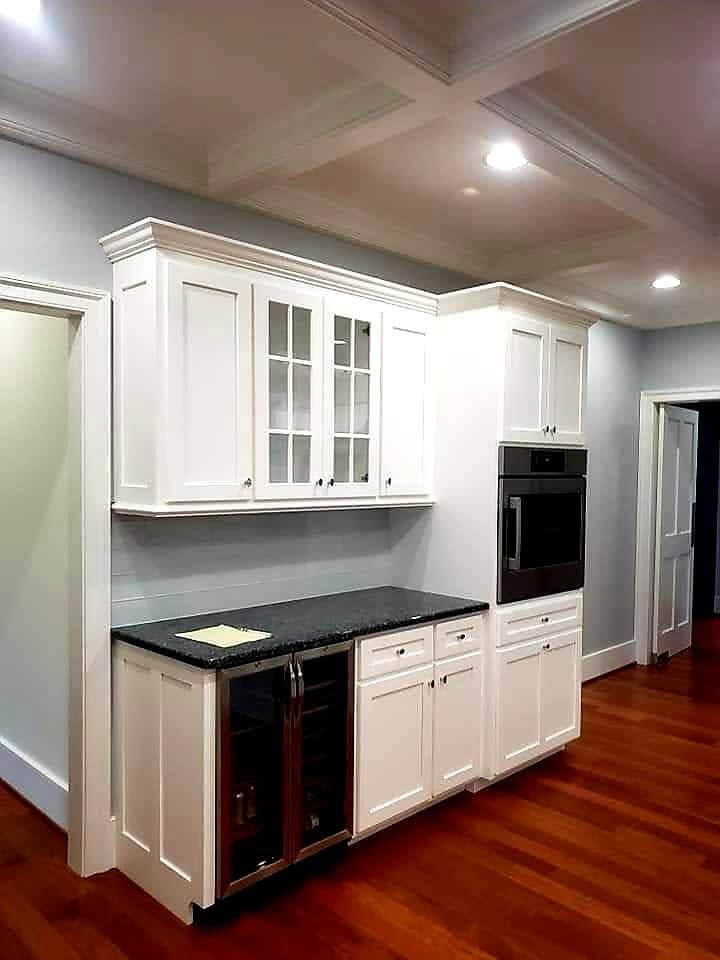 White built-in kitchen cabinets with black countertop and hardwood floors in an empty room.