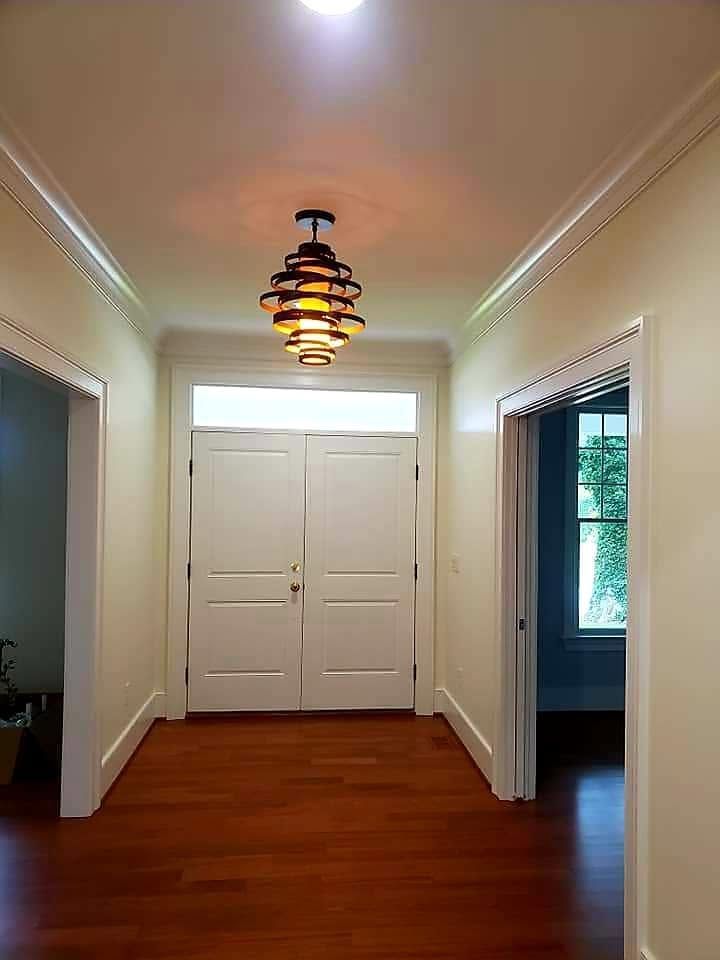 Hallway with white double doors, warm wood floor, and a hanging ceiling light.