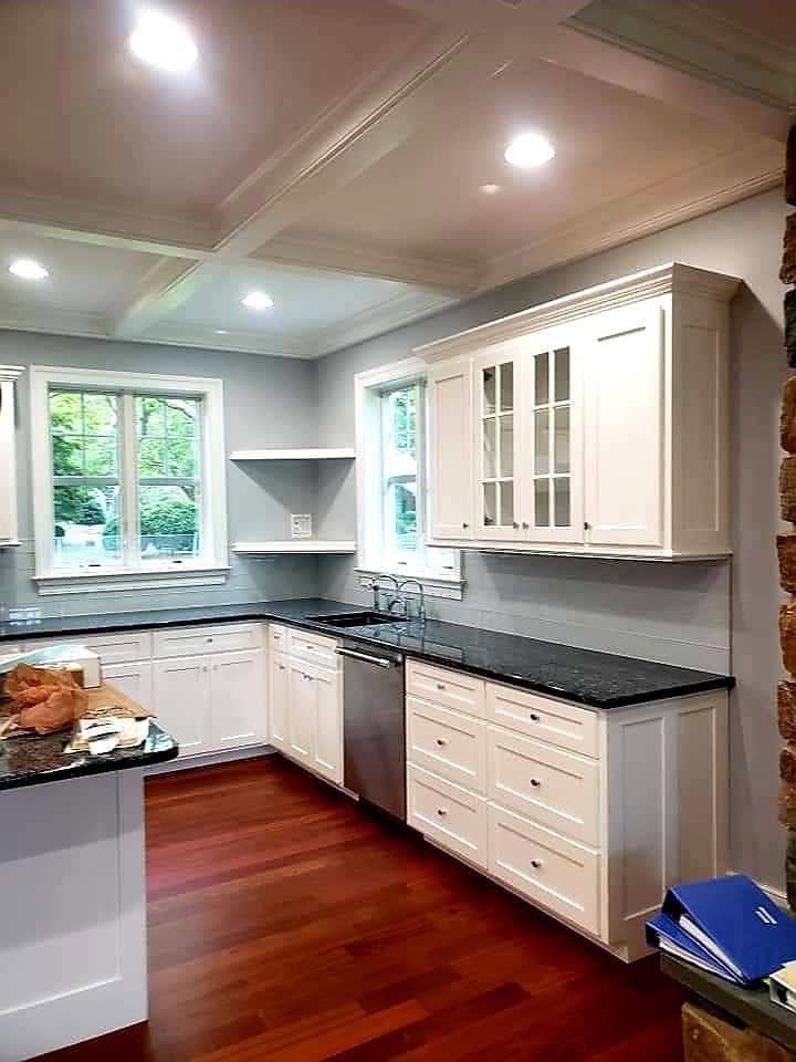 Bright modern kitchen with white cabinets, black countertops, red wood floors, and two windows.