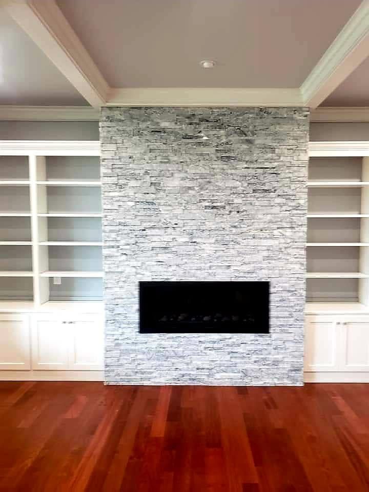 Modern living room with built-in white shelving, stone fireplace, and polished hardwood floors
